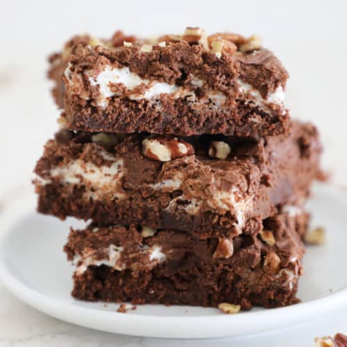 Three rocky road brownies stacked on a small white plate.