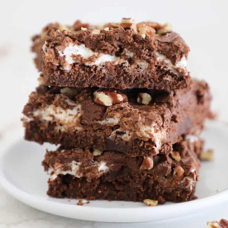 Three rocky road brownies stacked on a small white plate.