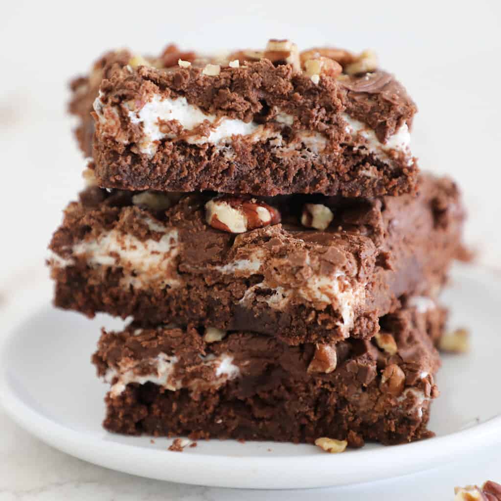Three rocky road brownies stacked on a small white plate. 
