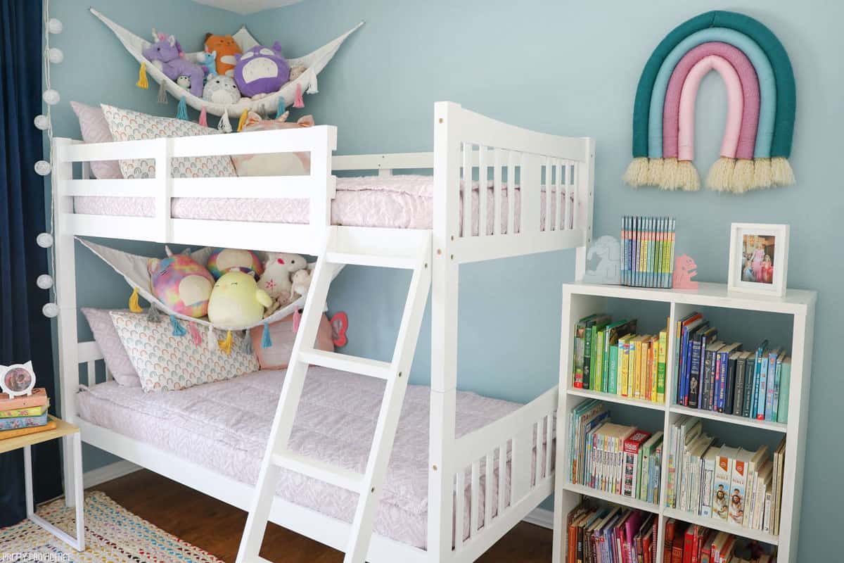 Girls bedroom with light blue walls, bunk bed, velvet curtains, stuffed animal hammocks and light purple bedding.