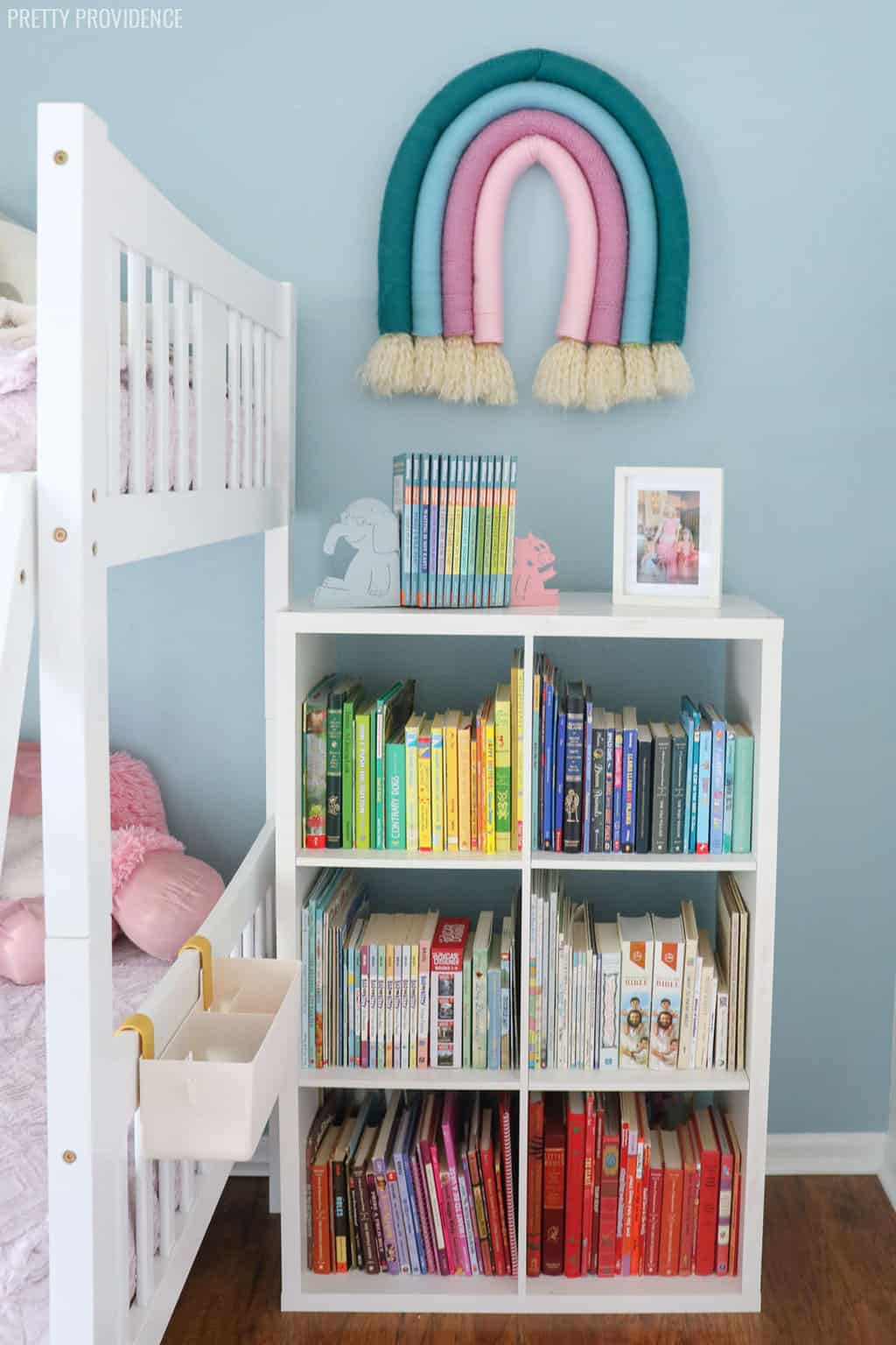 Girls bedroom with bookshelf organized by color, light blue walls.