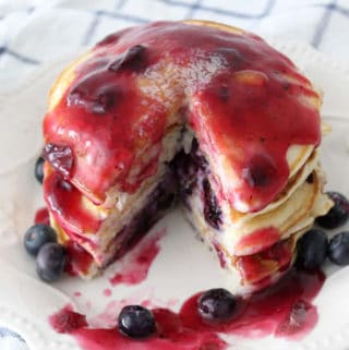A stack of blueberry pancakes with blueberry syrup and a wedge cut out of them.
