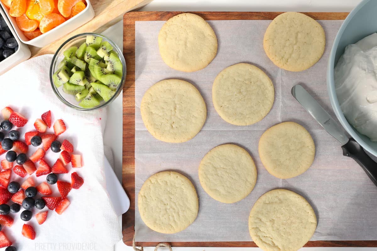 Sugar cookies on a cookie sheet, fresh fruit on the side.