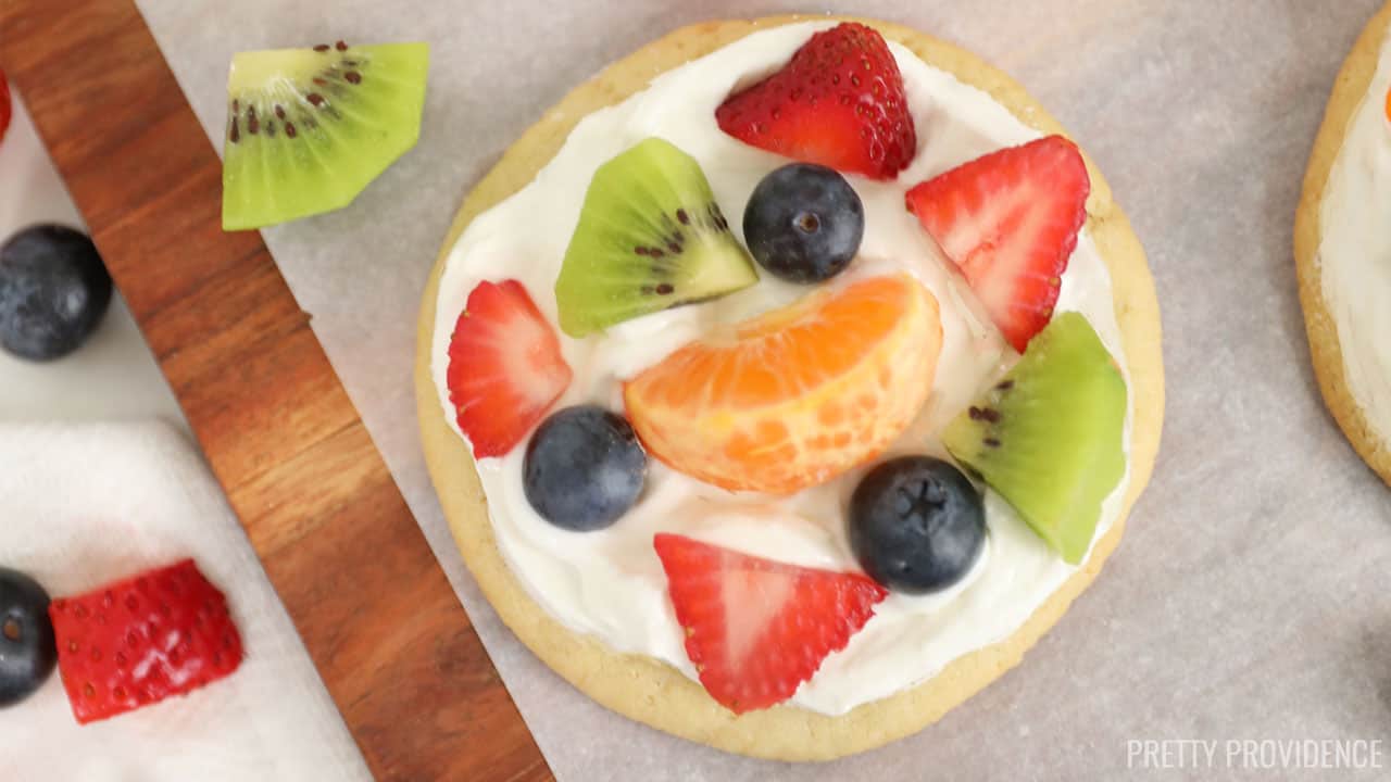 Mini fruit pizzas on sugar cookies, with frosting, sliced kiwi, blueberries, mandarin oranges and strawberries.