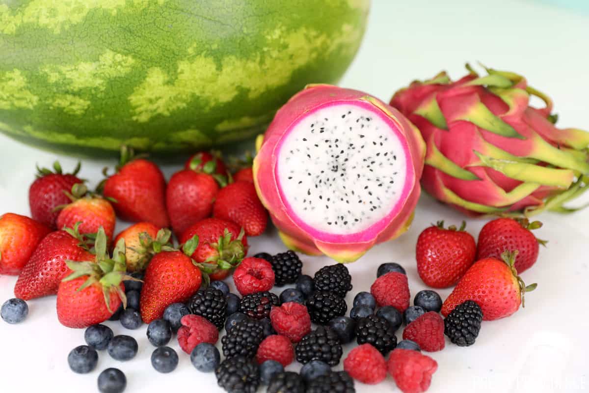 Watermelon, dragon fruit, strawberries, blueberries and raspberries on a white surface.