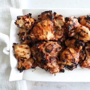Marinated grilled chicken thighs on a white platter.
