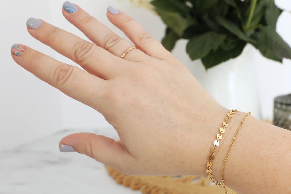 A photo of a womans hand and lower arm with two gold bracelets on it.