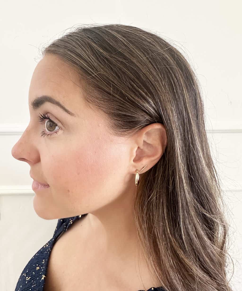 A side view of a womans face with eyes open and two gold earrings.