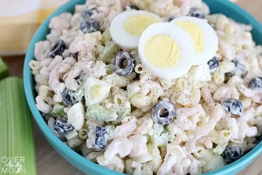 shrimp macaroni salad with olives and celery and hard-boiled eggs in a blue bowl.