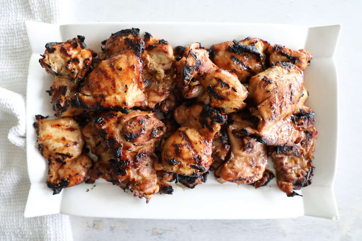 A white platter with grilled and marinated chicken thighs loaded on top.
