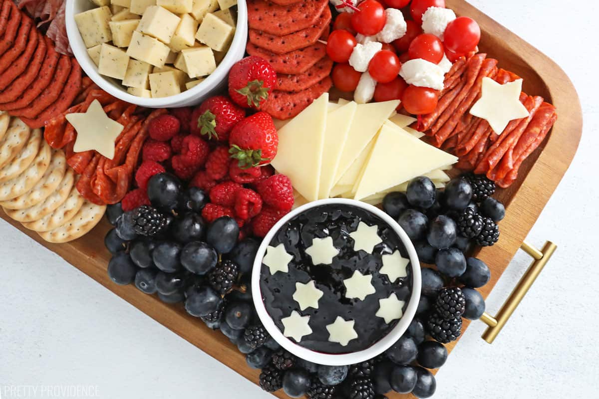 4th of July snacks on a charcuterie board with red, white and blue foods - crackers, meat, cheeses and fruit.