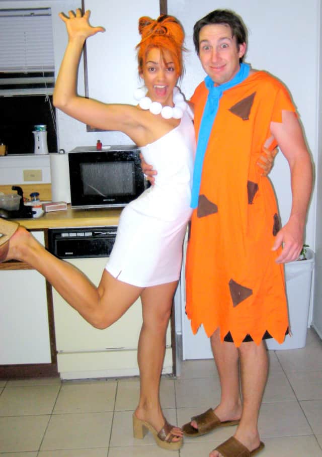 Woman and man wearing Wilma and Fred Flintstones Halloween costumes in a kitchen.