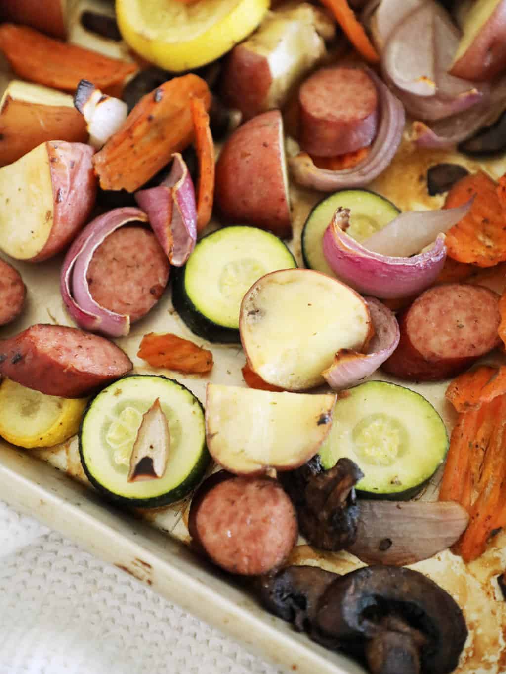 Corner view of a pan of roasted kielbasa and veggies.