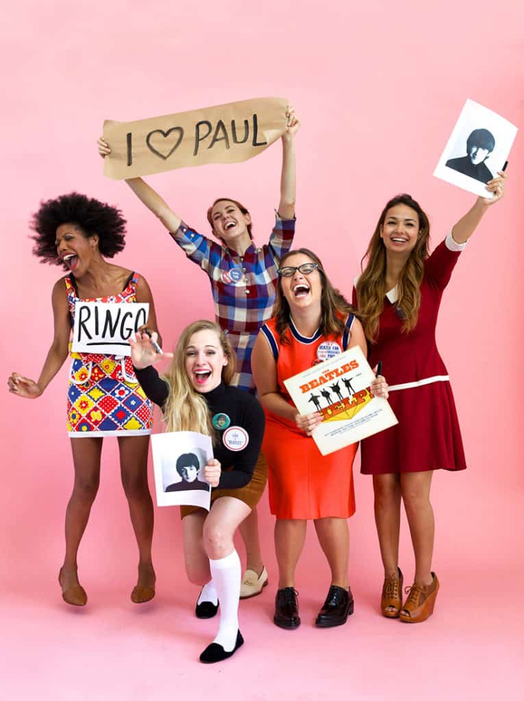 Women dressed up in 1960's clothing holding the beatles paraphernalia and signs as a beatles fan Halloween costume.