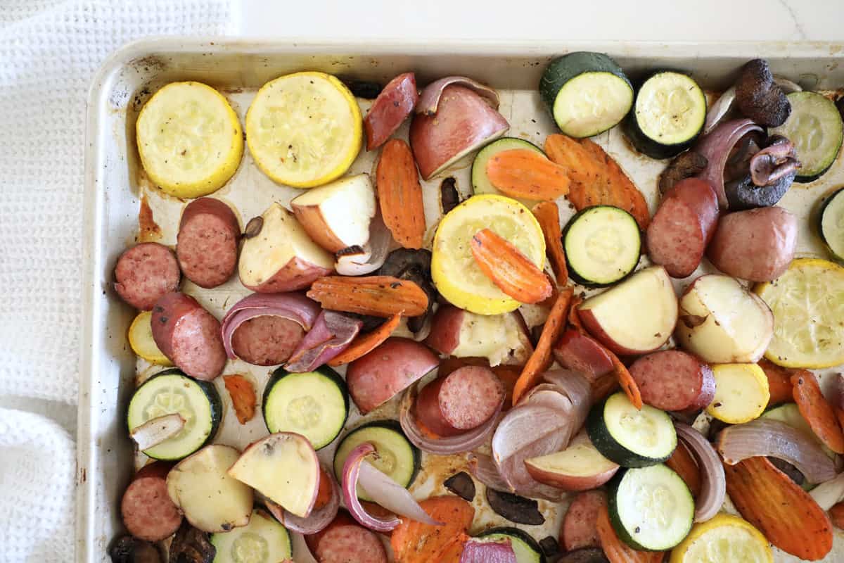 The corner of a sheet pan loaded with kielbasa and veggies.