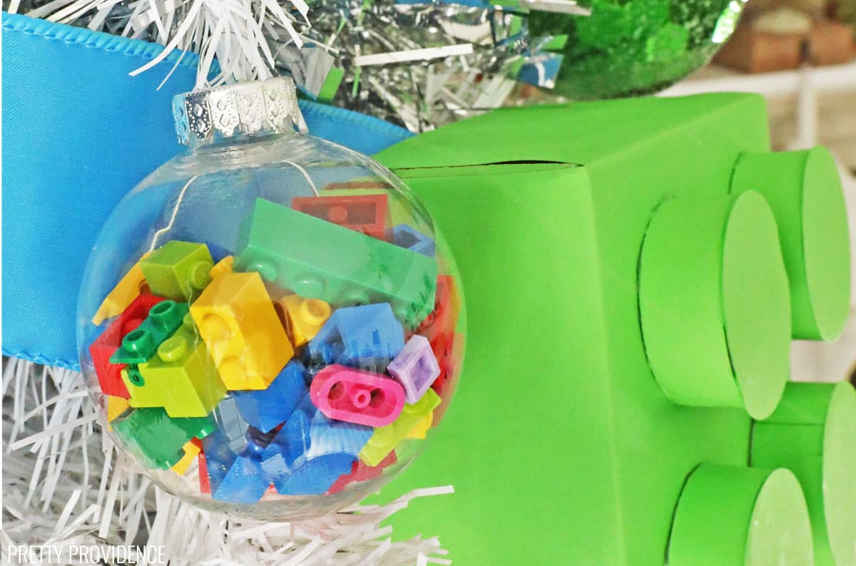 Clear christmas ornament filled with small colorful Lego bricks and a large lime green square Lego ornament on a white Christmas tree.