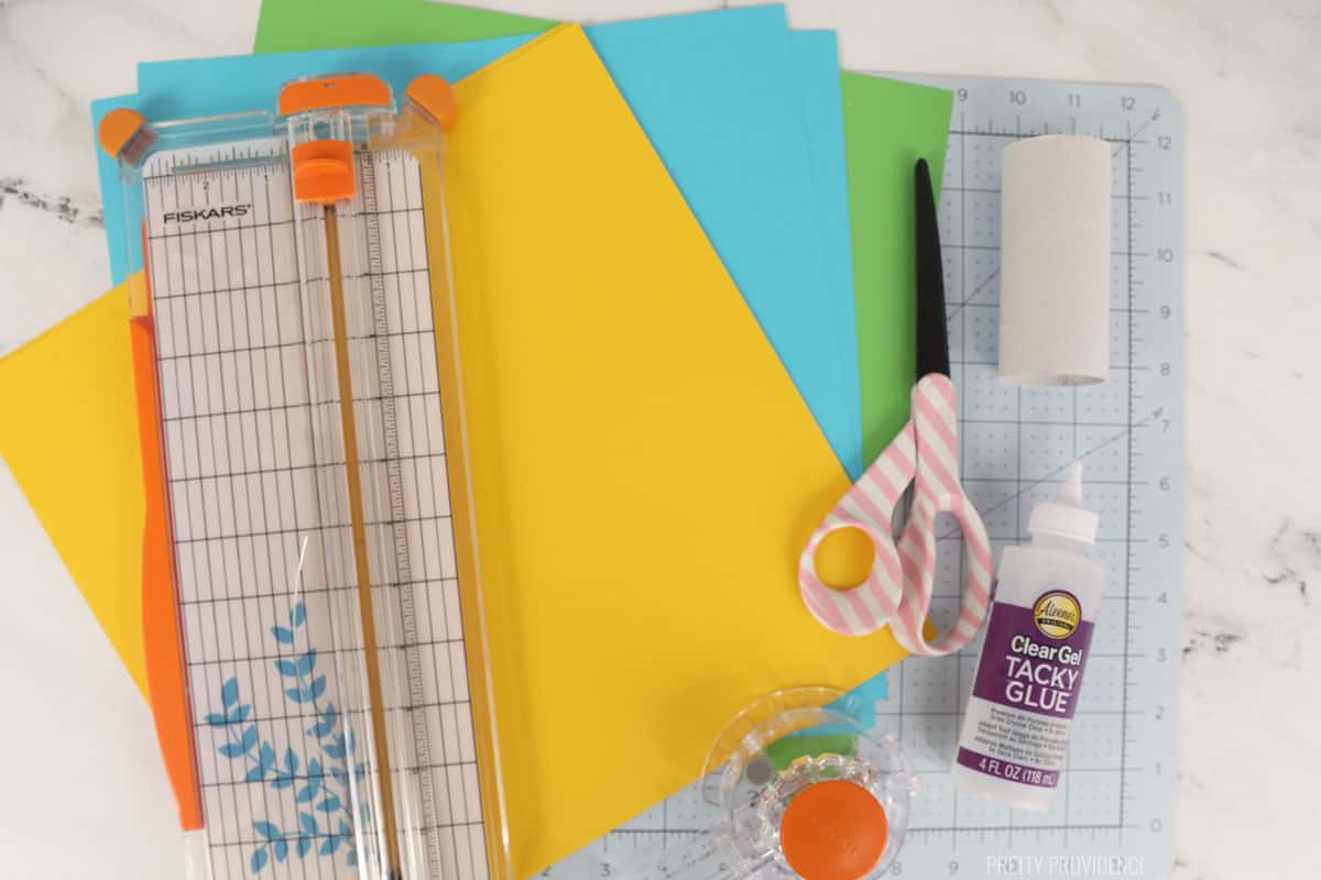 colorful paper, scissors, a paper cutter, tacky glue and a cutting mat. 