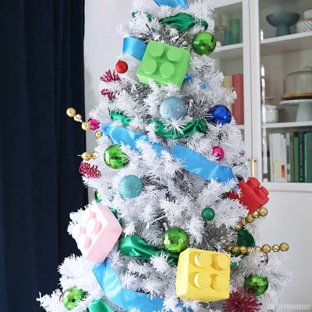 white Christmas tree with colorful lego christmas ornaments, colorful ball ornaments, and ribbon.
