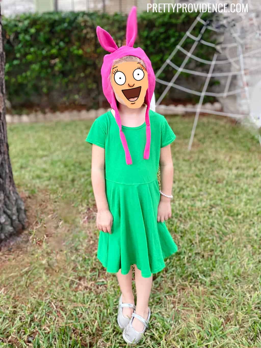 A kid dressed as Louise from Bob's Burgers wearing a green dress and a pink bunny ear hat..