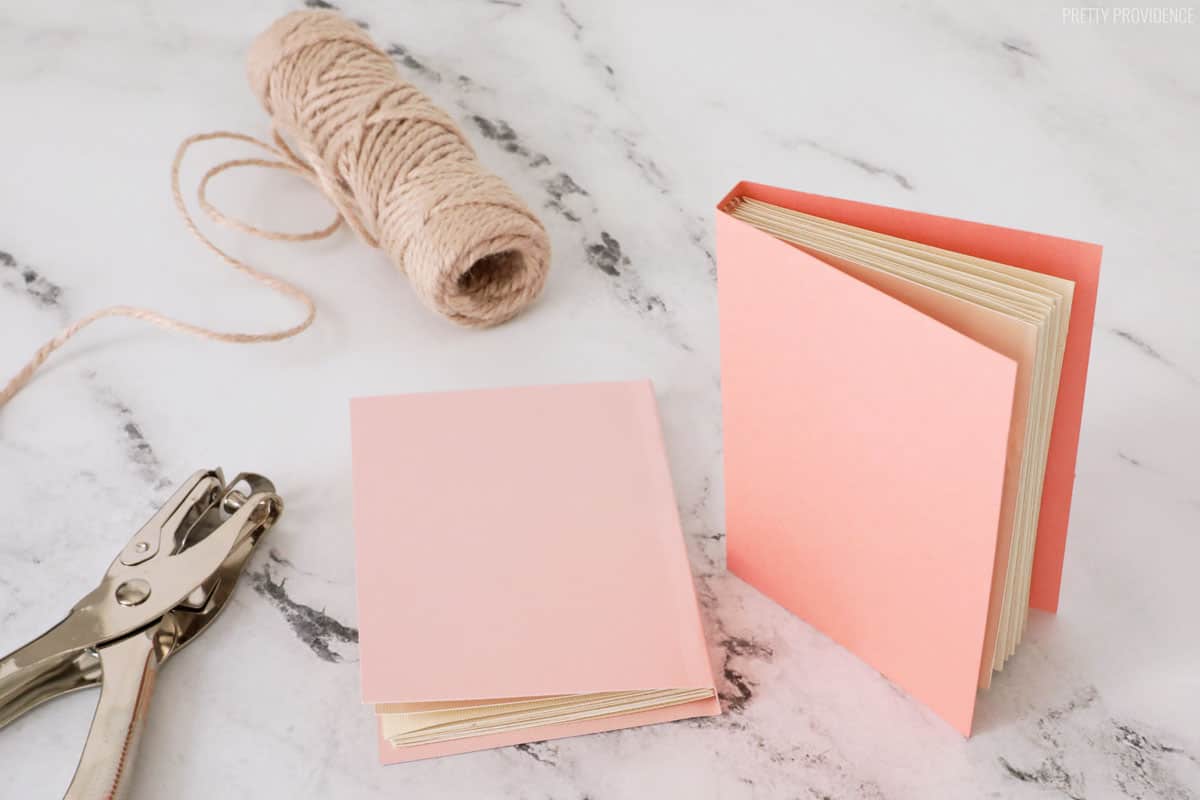 two mini pink books made out of card stock, a hole punch and a roll of twine.