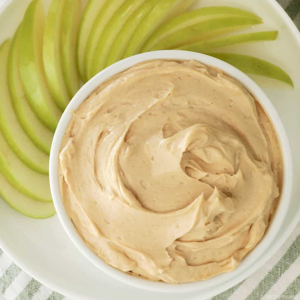 Apple dip in a white bowl with granny smith apple slices surrounding it.
