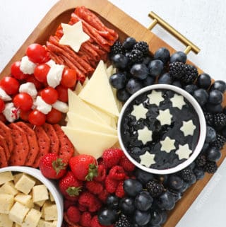 4th of July snacks on a charcuterie board with red, white and blue foods - crackers, meat, cheeses and fruit.