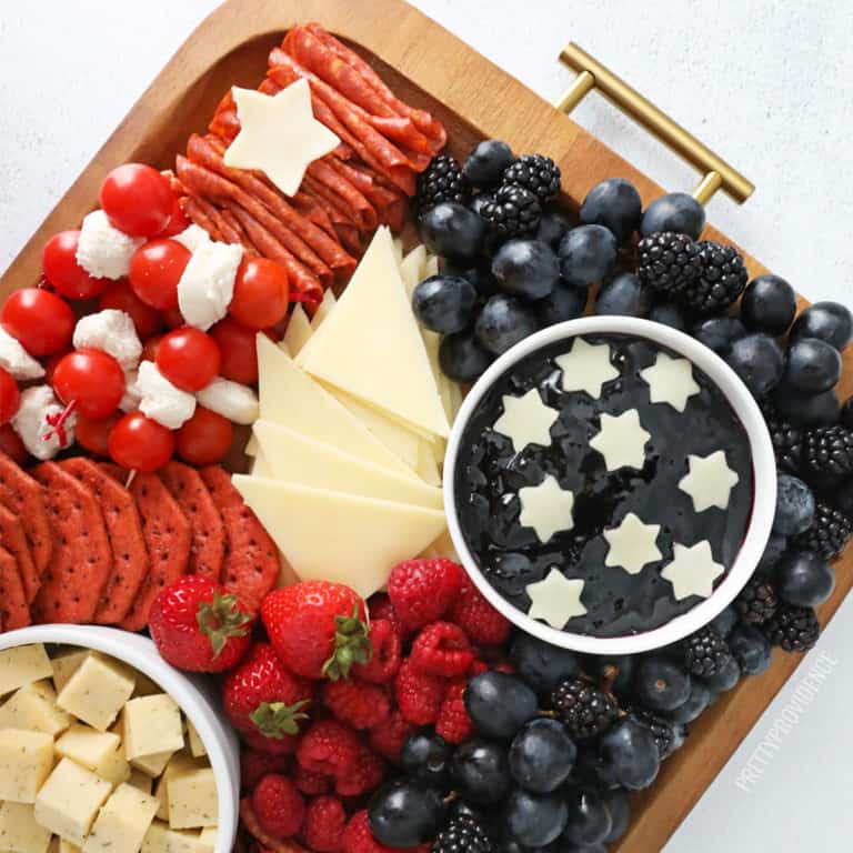 4th of July snacks on a charcuterie board with red, white and blue foods - crackers, meat, cheeses and fruit.