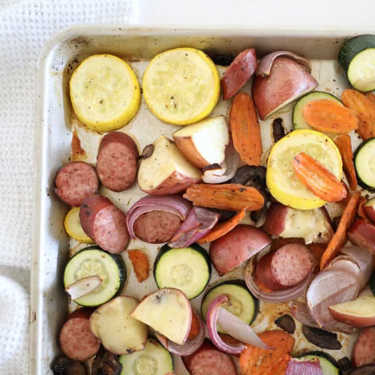 The bird's eye view of a corner of a sheet pan loaded with kielbasa and veggies.
