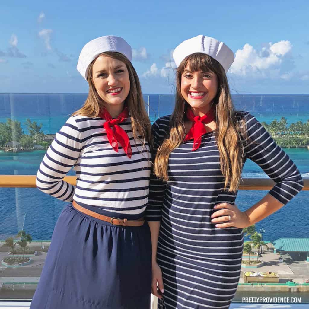 Sailor Costume on two women, one wearing a white and navy striped shirt with a navy skirt, red scarf and white sailor hat, another wearing a navy and white striped dress, white sailor hat and red scarf.