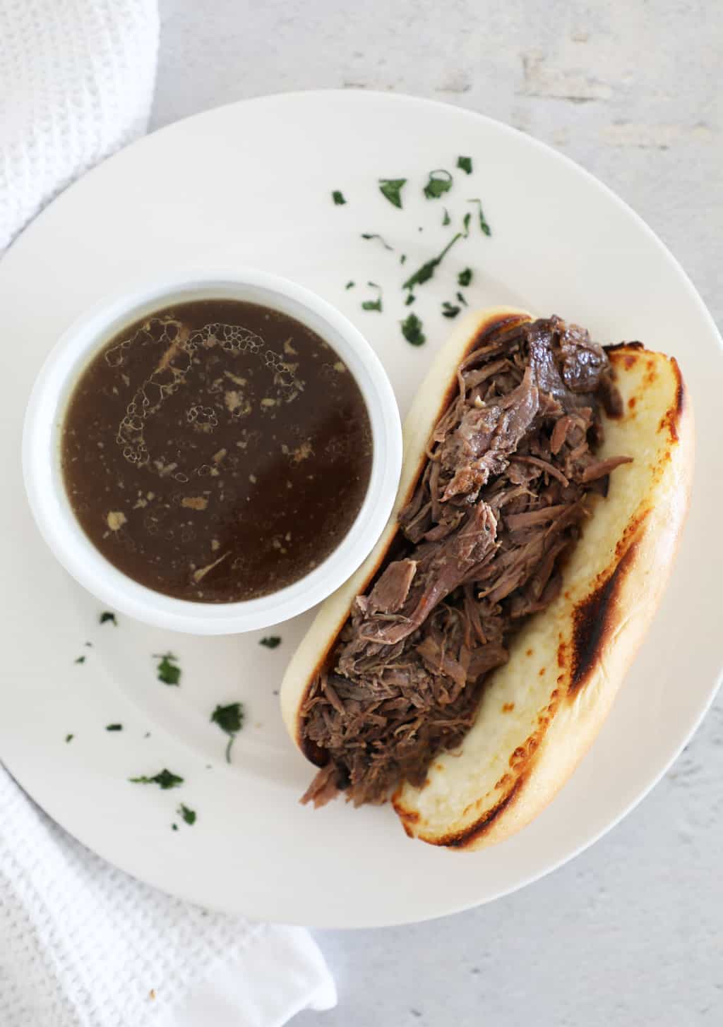 A bird's eye view of a crockpot French dip sandwich next to a small bowl of au jus. 