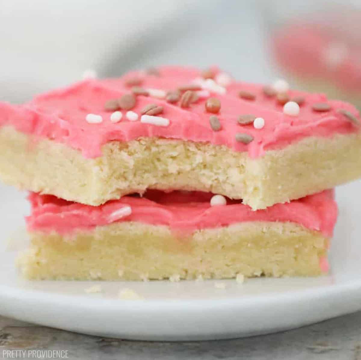 Sugar cookie bar with pink frosting and sprinkles on a small white plate. 