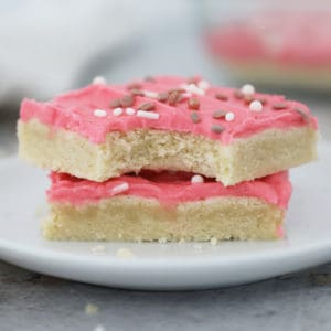Two sugar cookie bars with pink frosting on a small white plate.