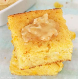 Two squares of Jiffy cornbread with creamed corn stacked on top of each other with a pat of melty honey butter on top.