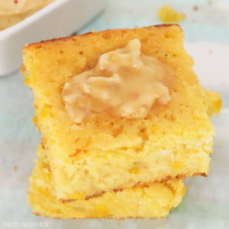 Two squares of Jiffy cornbread with creamed corn stacked on top of each other with a pat of melty honey butter on top.