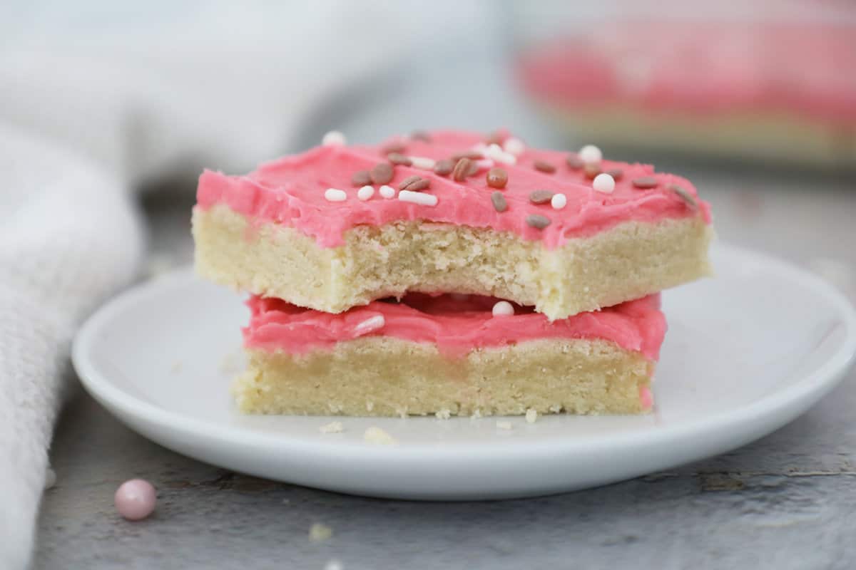 Two pink frosted sugar cookie bars on a small white plate. 