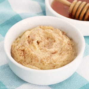 Whipped Honey Butter in a small white bowl with cinnamon sprinkled on top, a bowl of honey and a honey wand in the background.