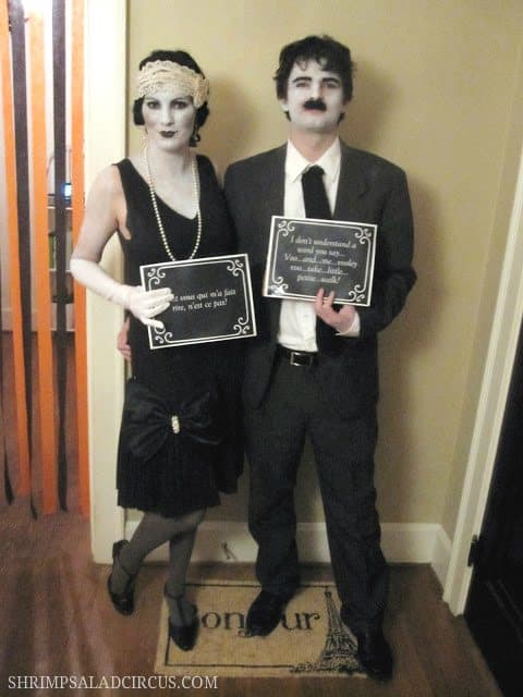 A couple dressed in 1920's fashion with gray makeup dressed up as silent film stars for Halloween.