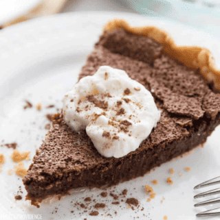 A slice of chocolate chess pie on a white plate with whipped cream on top, dusted with cocoa powder.