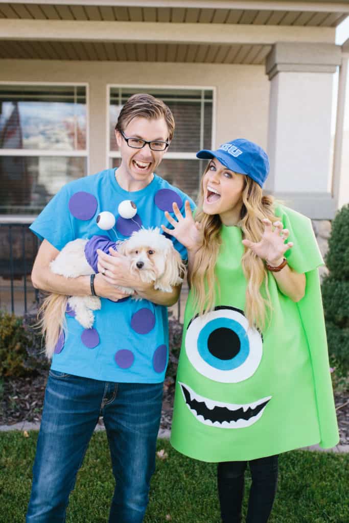 A woman and a man couples costume. The woman is dressed as Mike Wazowski and the man is dressed as Sulley and is holding a little dog in a monster costume.