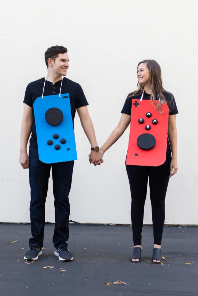 A man and woman dressed up in a couples nintendo switch costume. The man has a blue cardboard gaming control on his shirt, and the woman is wearing a red gaming control on her shirt, they are holding hands.