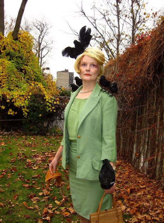 A woman in a green skirt suit with black birds on her head, shoulders, and arms. The Birds costume.