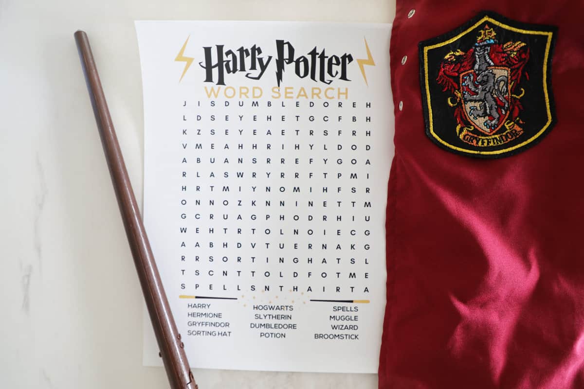A Harry Potter word search on the counter next to a wand and a cape.
