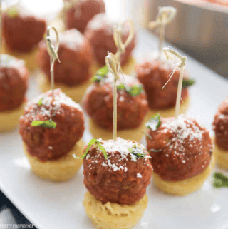Spaghetti nest with a meatball on top appetizer bites on toothpicks with parmesan and basil as garnish.