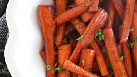 Close up bird's eye view of balsamic roasted carrots in a fancy white bowl.