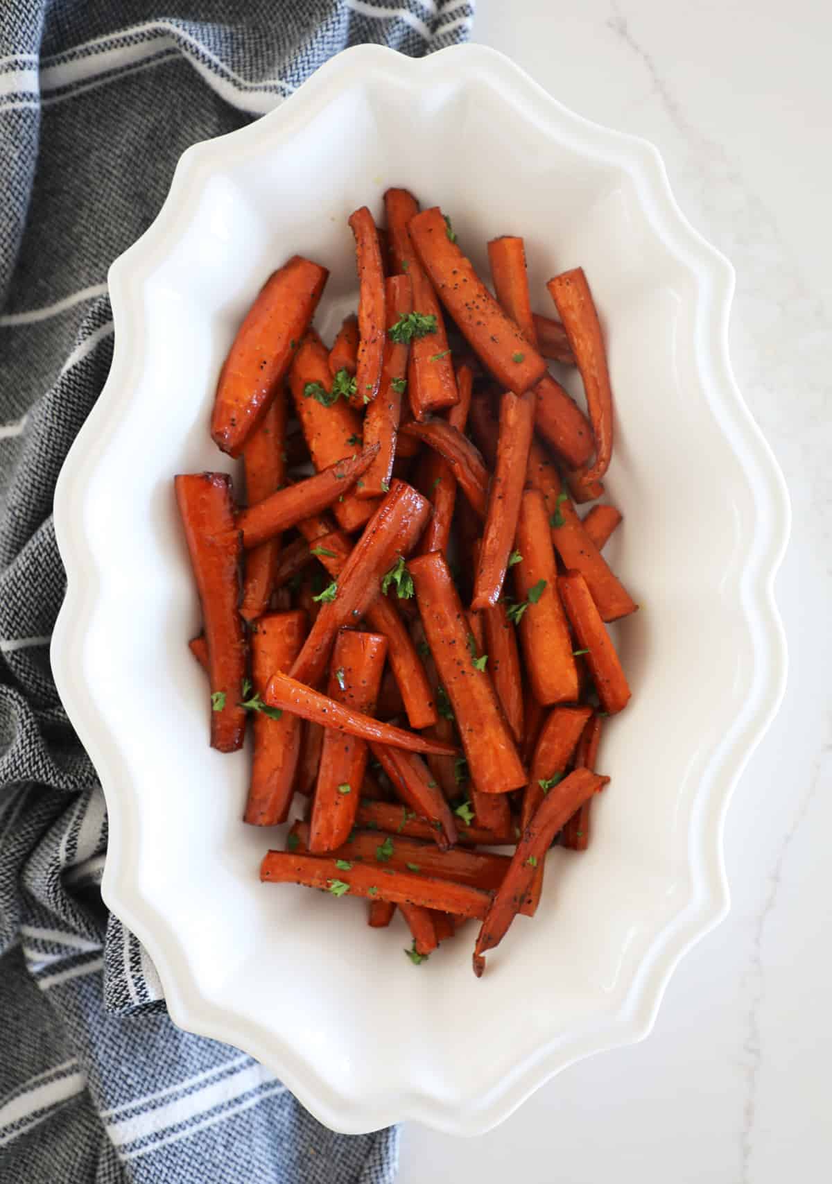 A decorative white bowl on a white counter filled with roasted balsamic carrots. 