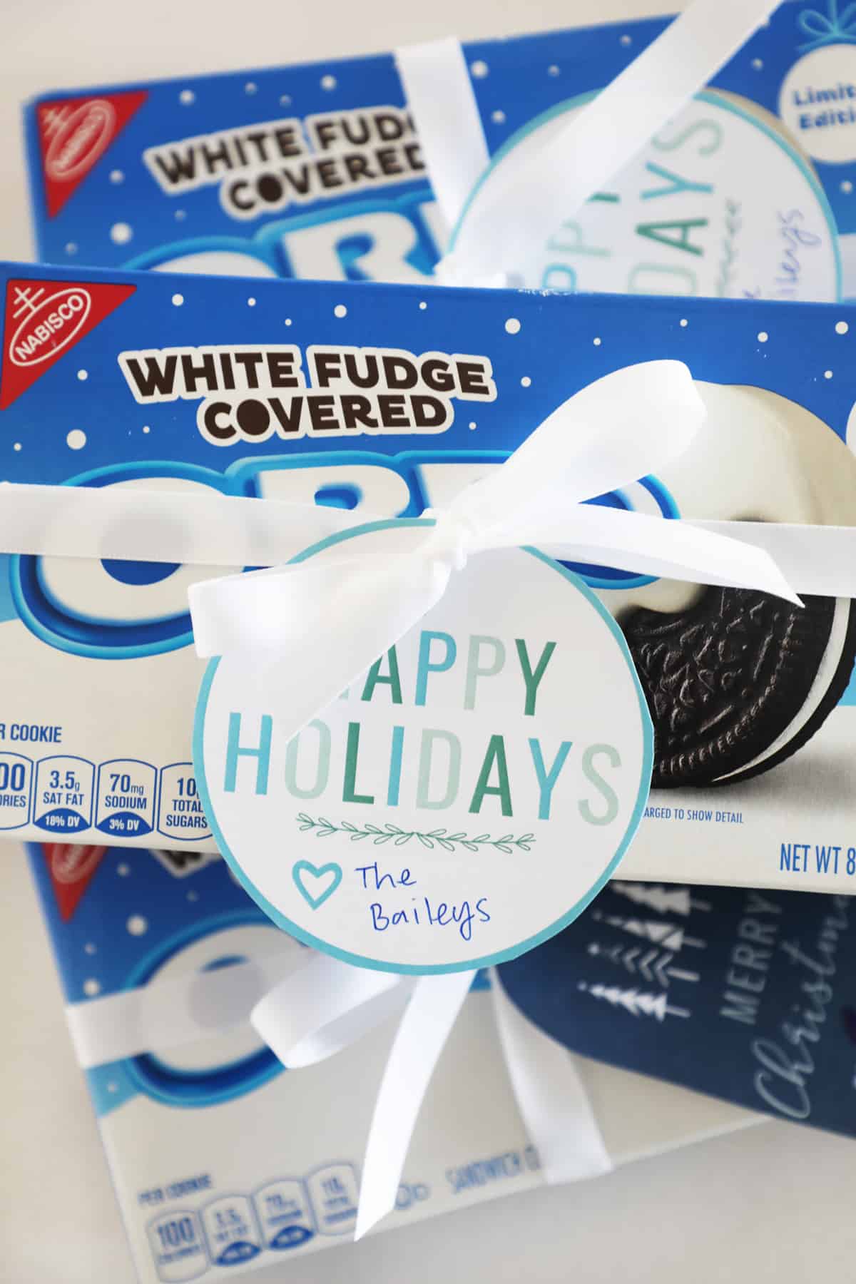 Three boxes of white chocolate covered Oreos with printable holiday gift tags tied on them with white ribbons.