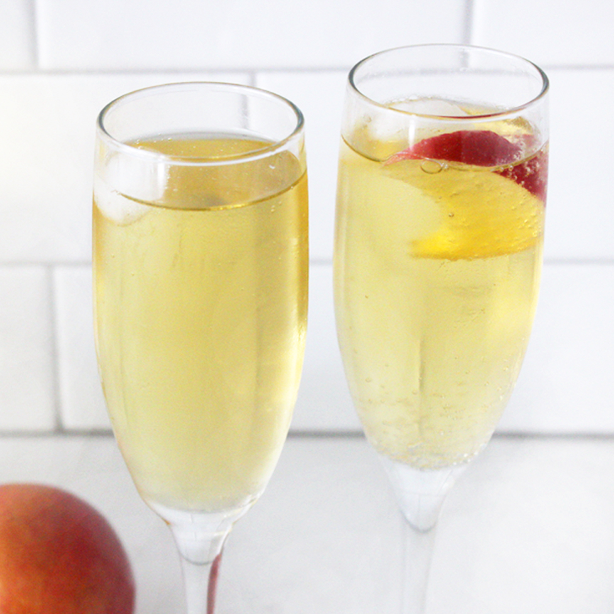 Two glasses of sparkling apple cider against a white backsplash.