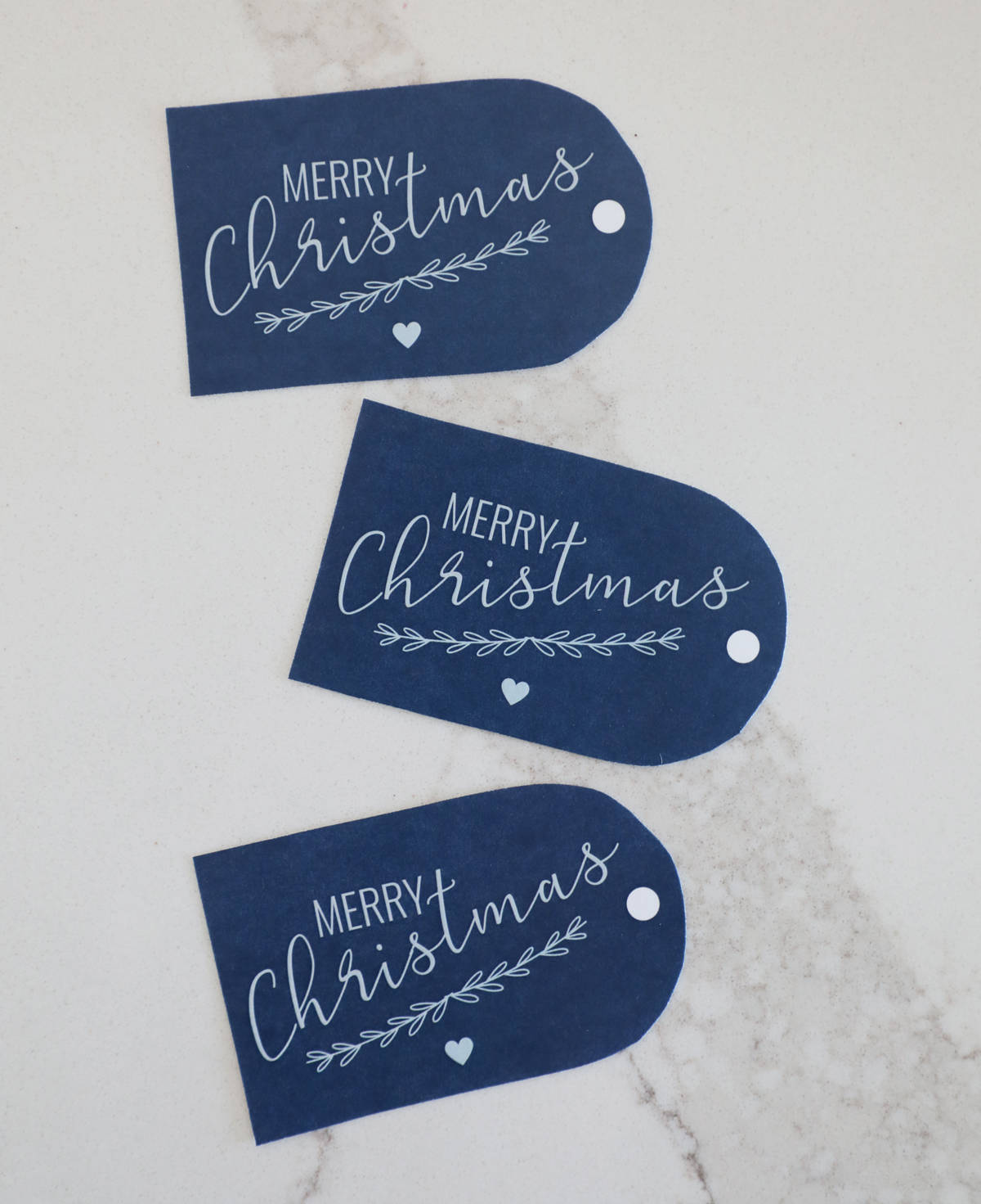 Three blue "Merry Christmas" printable gift tags on a white countertop. 
