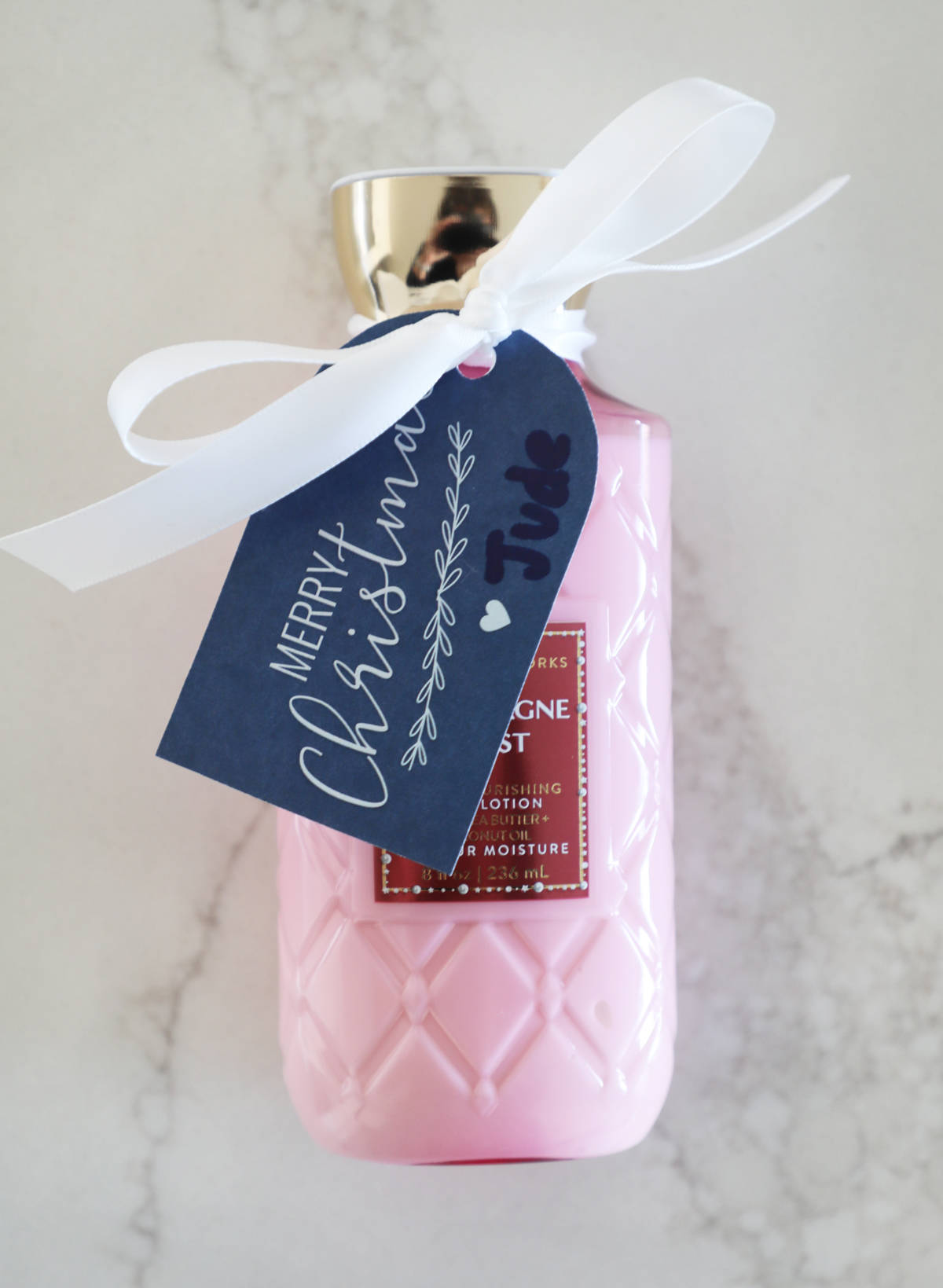 A free printable holiday gift tag tied to a bottle of pink lotion.
