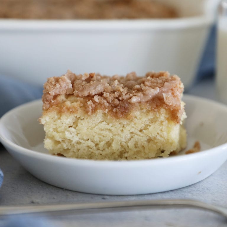 A slice of coffee cake on a small white dish with a fork in front of it.